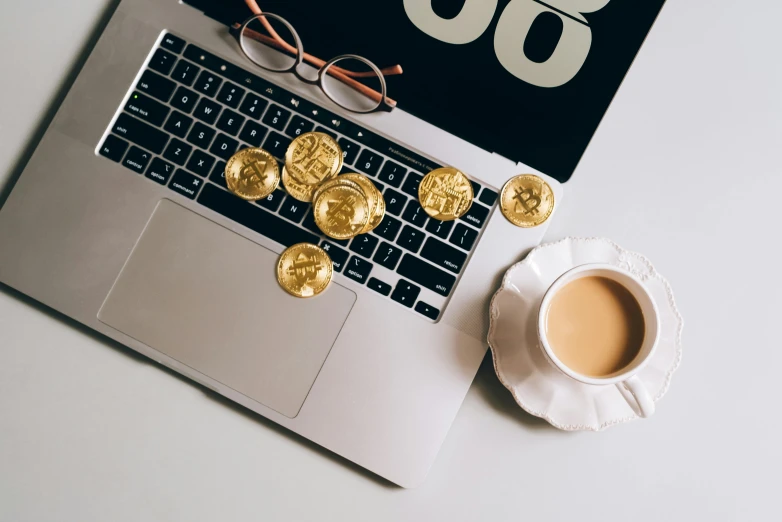 a laptop computer sitting on top of a table next to a cup of coffee, by Julia Pishtar, computer art, gold coins, 9 9 designs, edible crypto, thumbnail