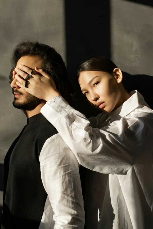 a man and a woman standing next to each other, an album cover, by irakli nadar, trending on unsplash, asian man, hands shielding face, at a fashion shoot, white sleeves