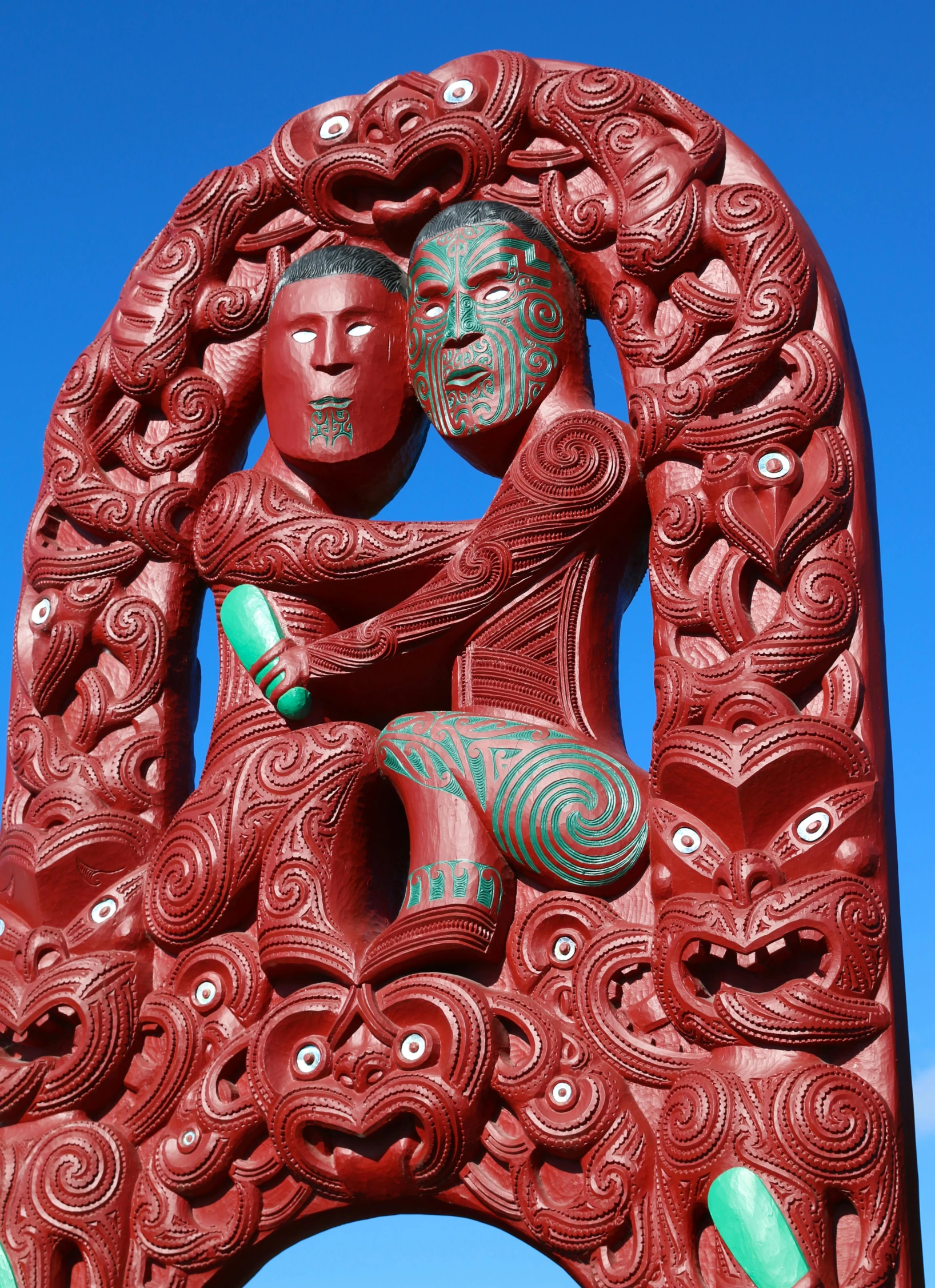 a red sculpture sitting on top of a lush green field, a statue, maori art, 2 people, slide show, devils