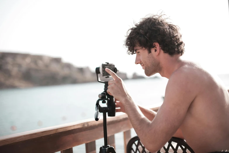 a man taking a picture of a body of water, by Daniel Seghers, pexels contest winner, happening, young greek man, home video footage, tripod, lean man with light tan skin