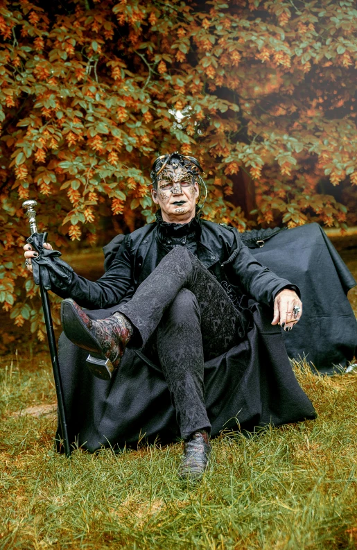 a man sitting in a chair in the grass, an album cover, pexels, renaissance, gothic coat, full body with costume, autum, male drow