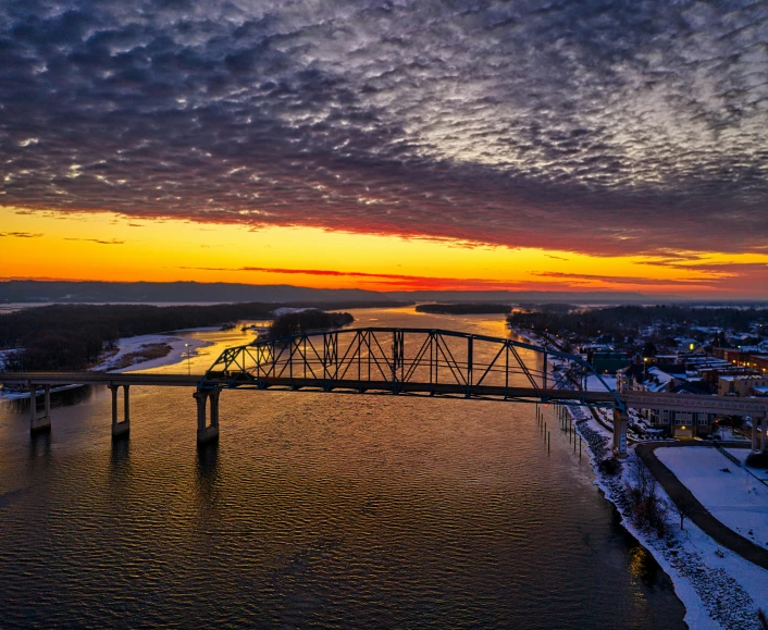 a bridge over a body of water under a cloudy sky, by Rob Alexander, pexels contest winner, cold sunset, drone photograpghy, midwest town, thumbnail