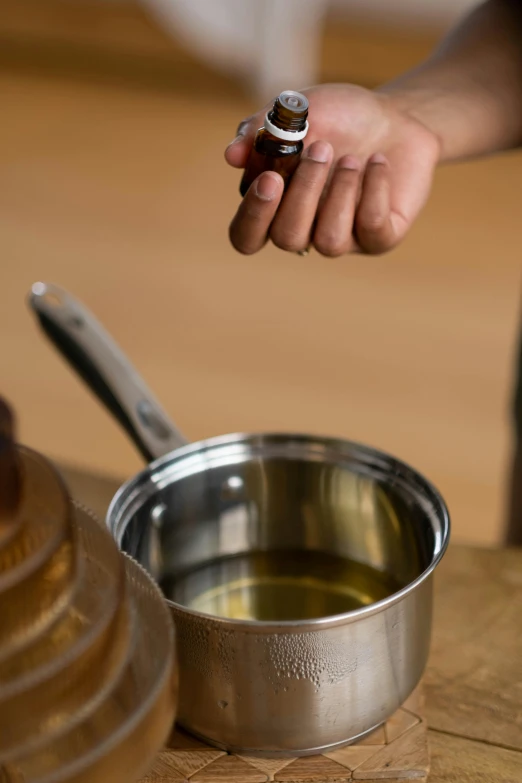 a close up of a person holding a bottle of oil, pot, thumbnail, stainless steel, brown