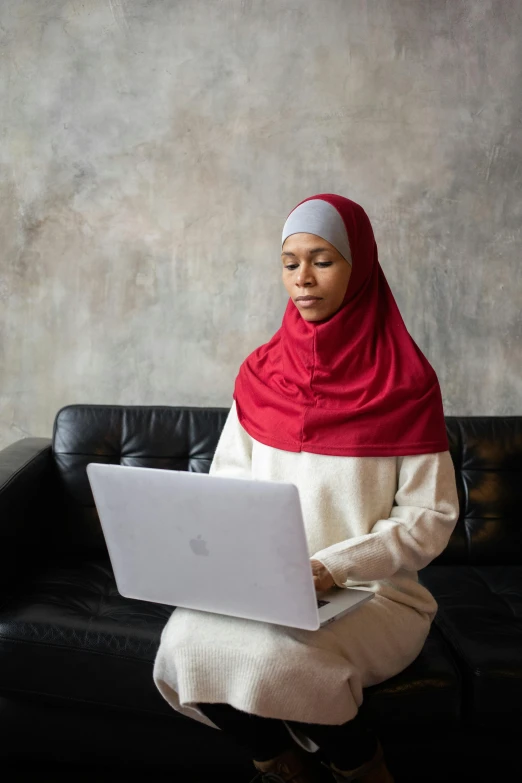 a woman sitting on a couch using a laptop, inspired by Maryam Hashemi, hurufiyya, maroon and white, wearing red attire, malaysian, protective