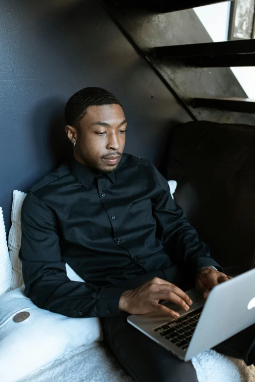 a man sitting on a bed using a laptop computer, by Cosmo Alexander, trending on unsplash, renaissance, black shirt, panel of black, office clothes, mkbhd as iron man