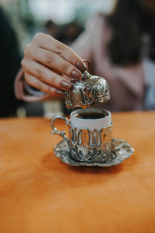 a person sitting at a table with a cup of coffee, arabesque, made out of shiny silver, vintage vibe, istanbul, instagram story