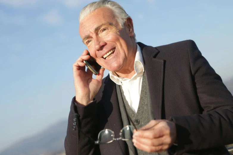 a man in a suit talking on a cell phone, by John Murdoch, pexels, white-haired, sunny sky, actor, selling insurance