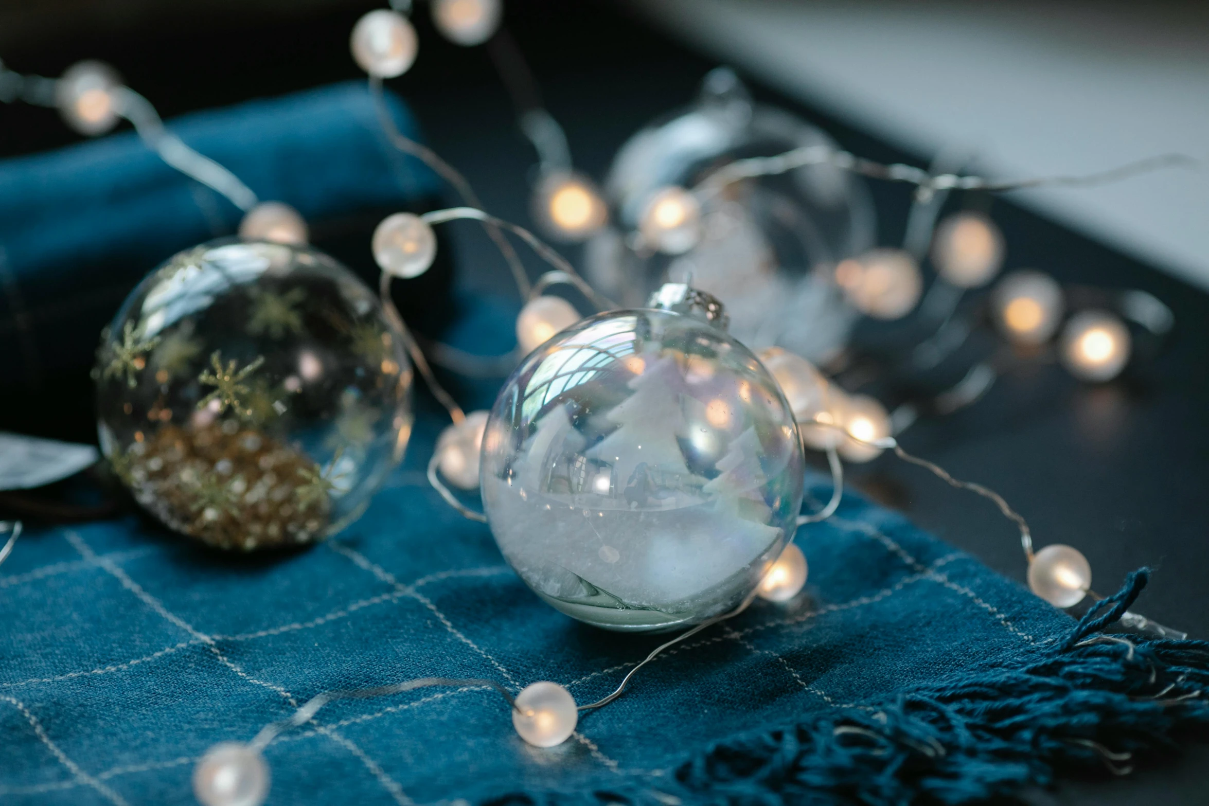 a table topped with christmas ornaments on top of a blue cloth, inspired by Bruce Munro, unsplash, soap bubble, string lights, close-up product photo, silver，ivory