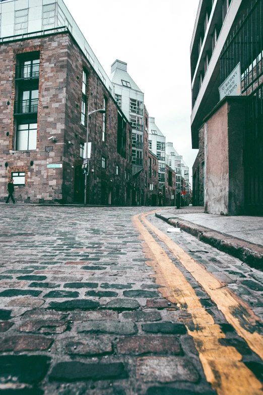 a cobblestone street with buildings in the background, inspired by Elsa Bleda, pexels contest winner, scottish style, industrial aesthetic, flattened, vibrant but dreary gold