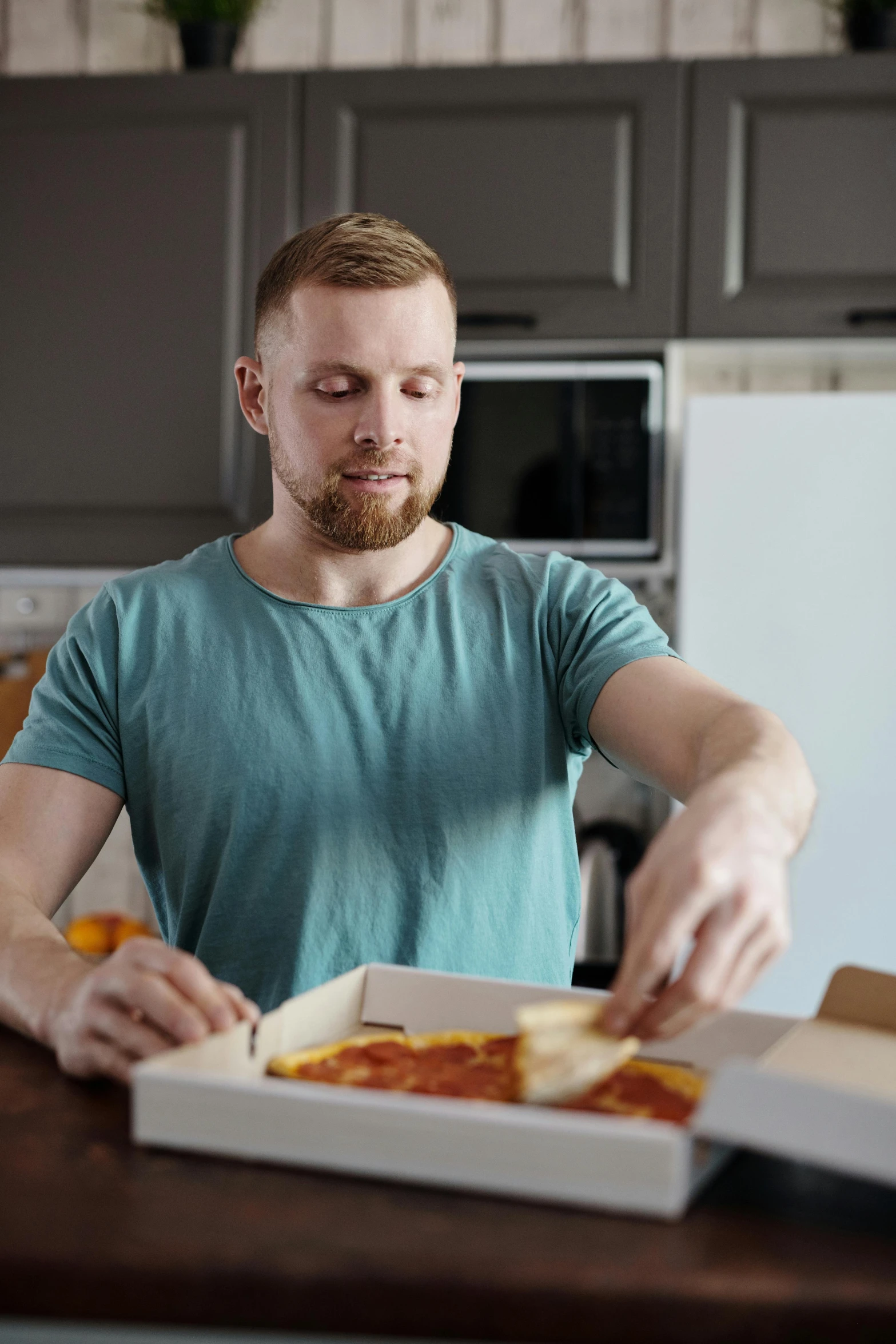 a man sitting at a table with a box of pizza, in a kitchen, hziulquoigmnzhah, extra crisp image, rectangle