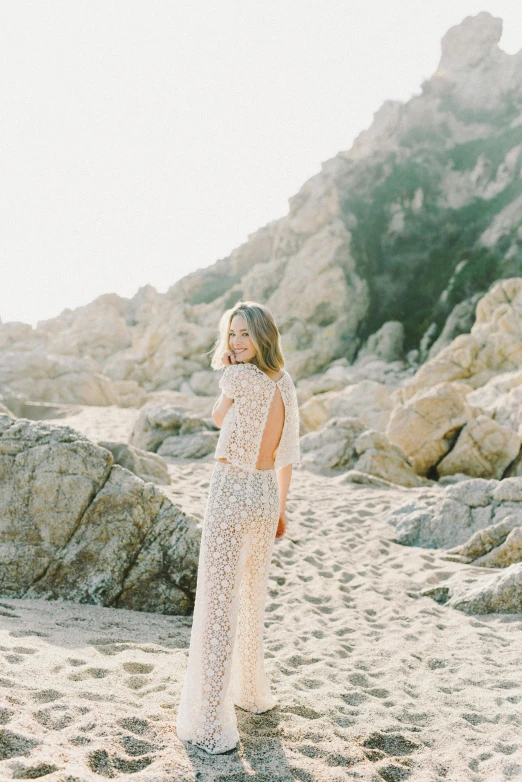 a woman standing on top of a sandy beach, intricate gown, open back dress, zoomed in shots, standing on rocky ground