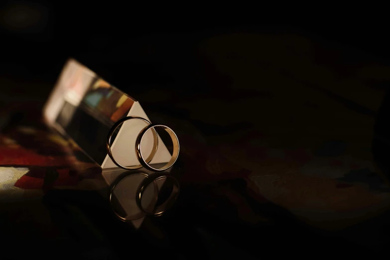 a pair of wedding rings sitting on top of a table, inspired by Anna Füssli, crystal cubism, art photograph, inlaid with gold, dark vignette, close up shot from the side