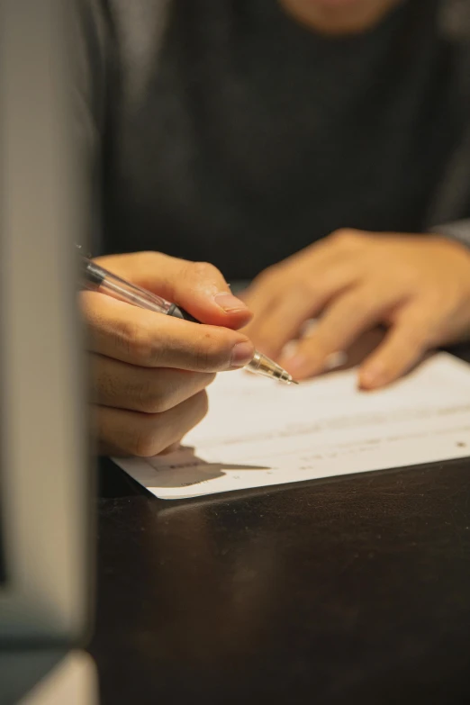 a person sitting at a table writing on a piece of paper, sleek hands, high-quality photo, digital image, lgbtq