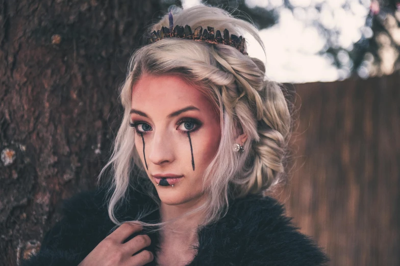 a woman with a crown on her head next to a tree, inspired by Elsa Bleda, trending on pexels, renaissance, crying makeup, jessica nigri face!!, female viking, black feathers instead of hair