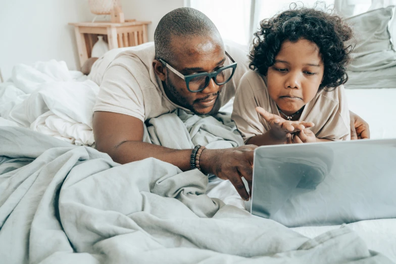 a man and woman laying in bed looking at a laptop, a cartoon, pexels, father with child, black man, instagram photo, reading