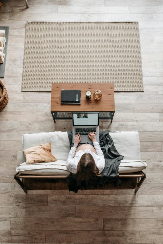 a woman sitting on a couch using a laptop, pexels contest winner, herringbone floor, sustainable materials, shot from a drone, brown and white color scheme