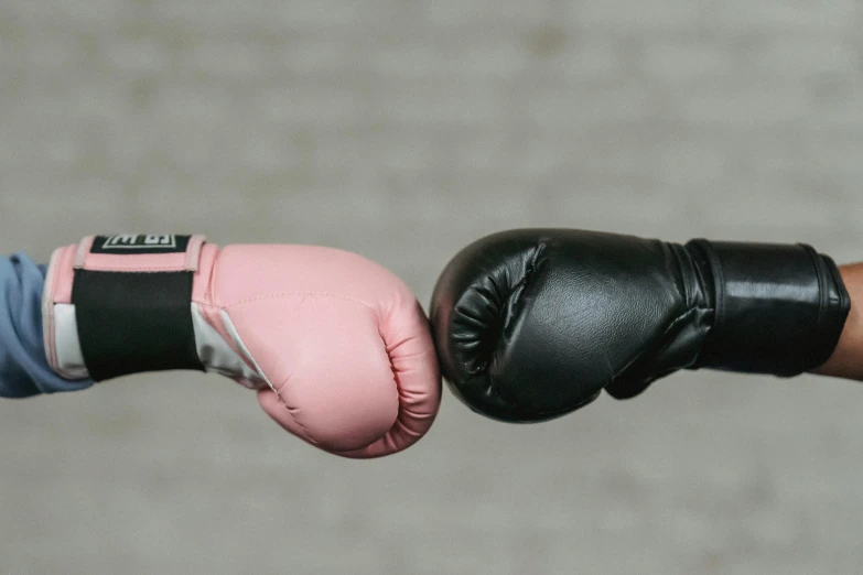 a close up of two people wearing boxing gloves, pink and black, reaching out to each other, black gloves, top selection on unsplash