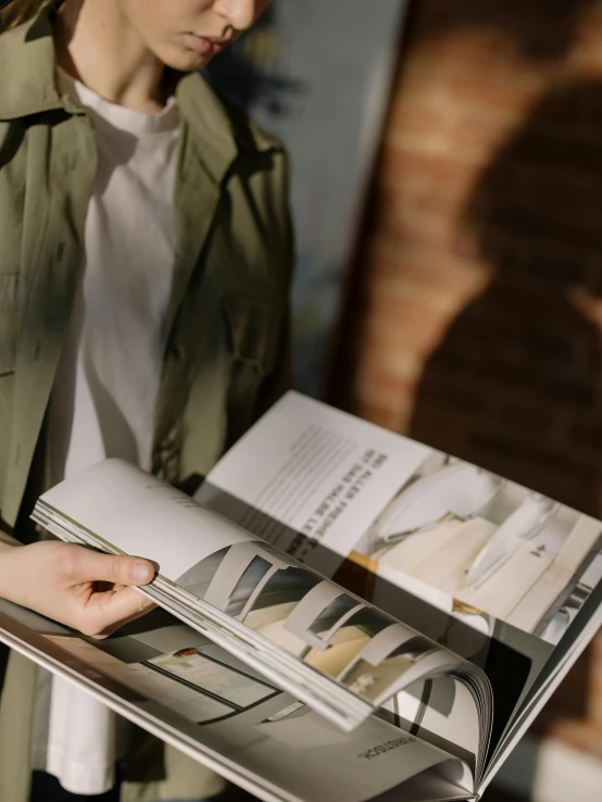 a woman in a green jacket holding a book, trending on unsplash, visual art, clippings of a fashion magazine, wearing a light shirt, low angle photo, carrying a tray