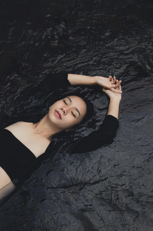 a woman laying on top of a body of water, an album cover, inspired by Ren Hang, unsplash contest winner, with a black dark background, relaxed expression, asian women, dry skin