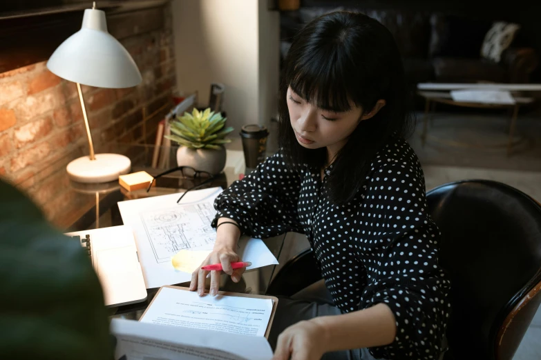 a woman sitting at a table reading a book, by Jang Seung-eop, pexels contest winner, writing on a clipboard, gemma chan, in office, hikkikomori