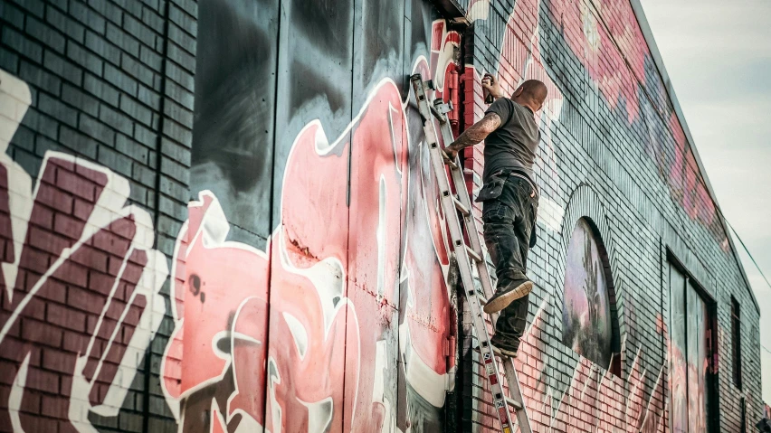 a man on a ladder painting on the side of a building, by Lee Loughridge, pexels contest winner, graffiti, it has a red and black paint, istock, thumbnail, mechanic