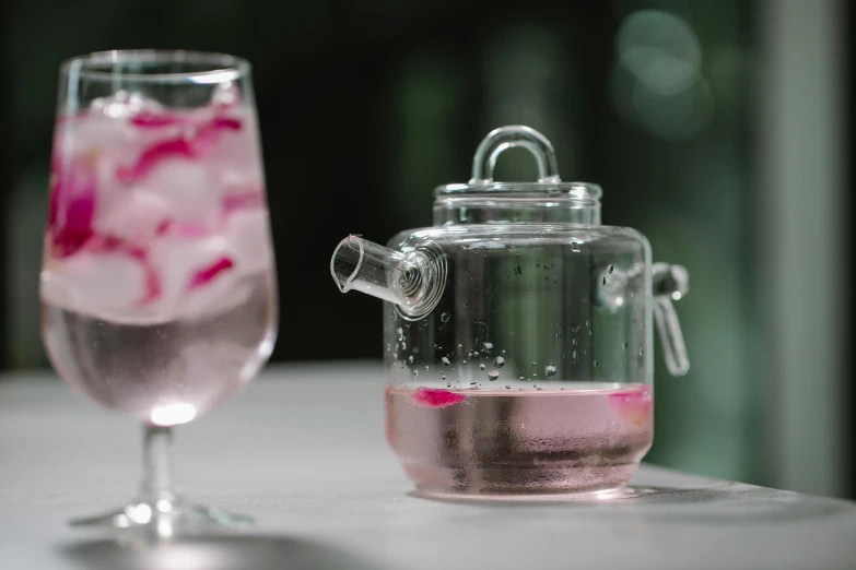 a glass filled with pink liquid next to a glass of water, a still life, unsplash, teapot, al fresco, grey, close-up shot from behind