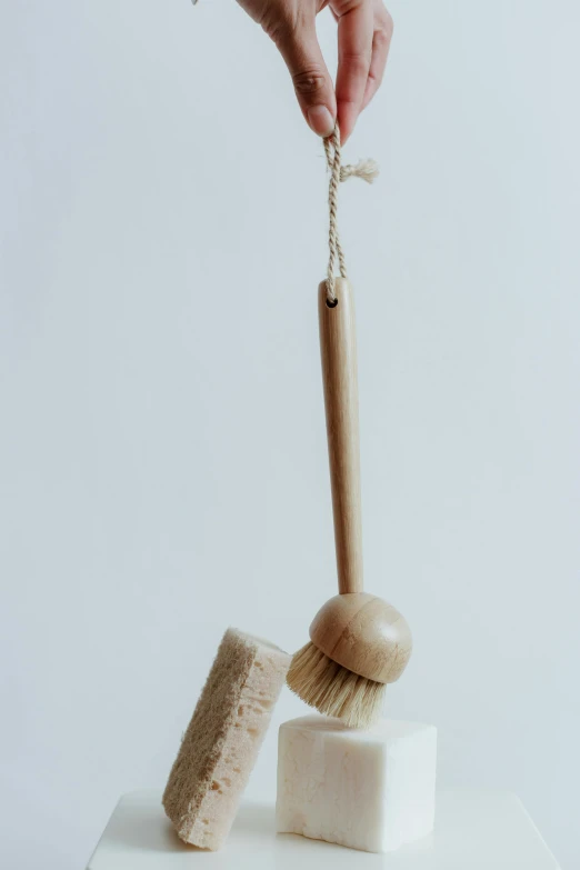 a person holding a brush on top of a cake, unsplash, purism, hanging rope, natural materials, beige, wash