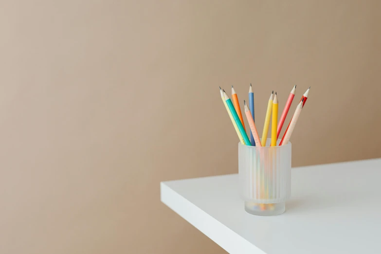 a glass filled with colored pencils on top of a white table, by Rachel Reckitt, minimalism, muted rainbow tubing, background image, glossy white metal, beige sky pencil marks
