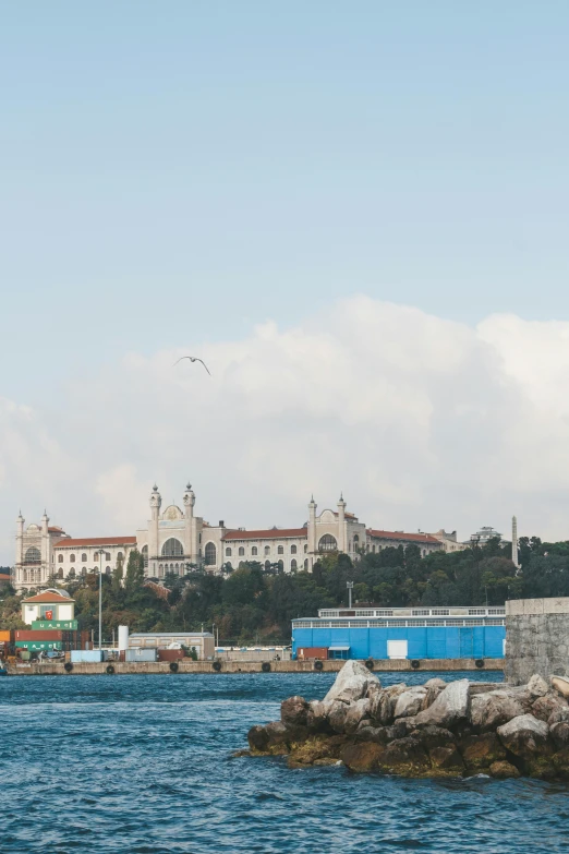 a lighthouse sitting on top of a rock in the middle of a body of water, a colorized photo, inspired by Almada Negreiros, renaissance, hospital in background, city walls, seen from a distance, shot on sony a 7 iii