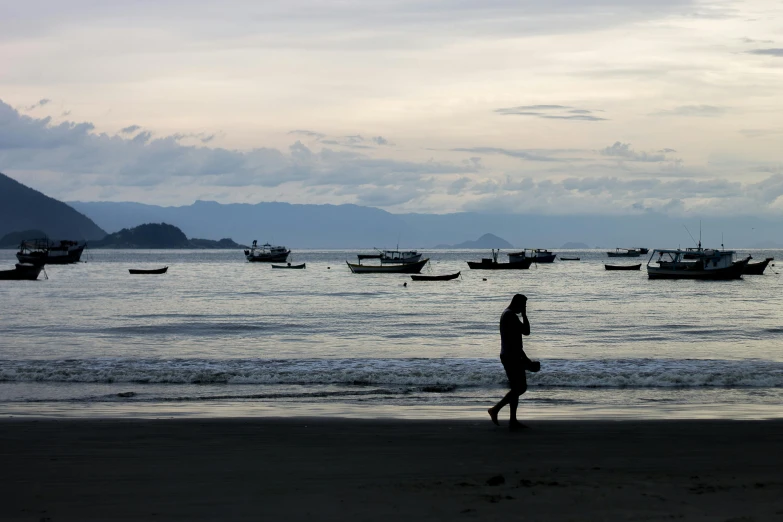 a person walking on a beach near a body of water, inspired by Steve McCurry, sumatraism, boats, silhouetted, street photo, thumbnail