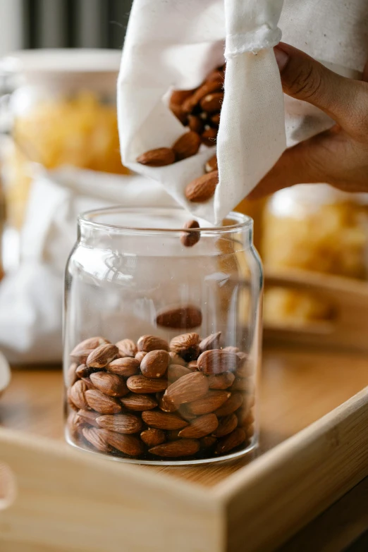 a person pouring almonds into a glass jar, by Jessie Algie, 6 pack, medium, recipe, silk