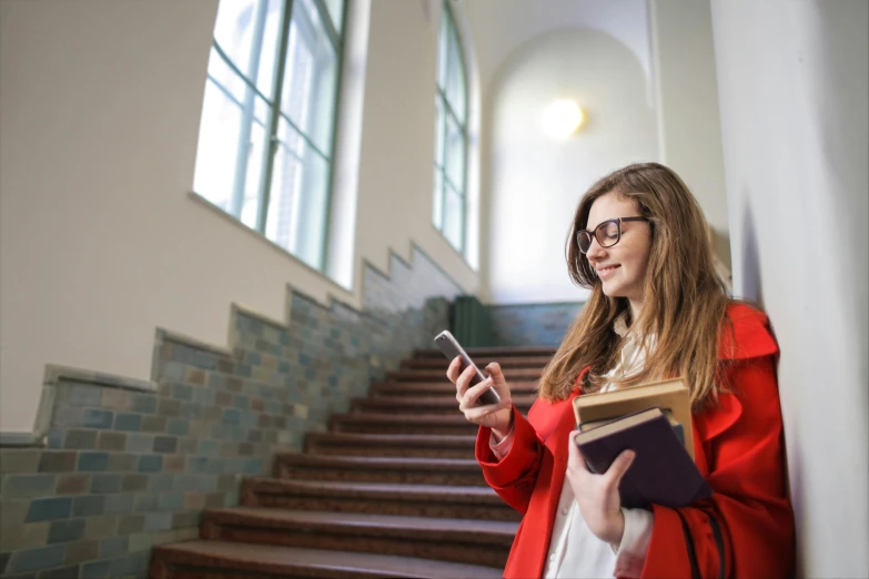 a woman in a red coat holding a book and a cell phone, at college, ui and ux, inside a grand, teenage girl