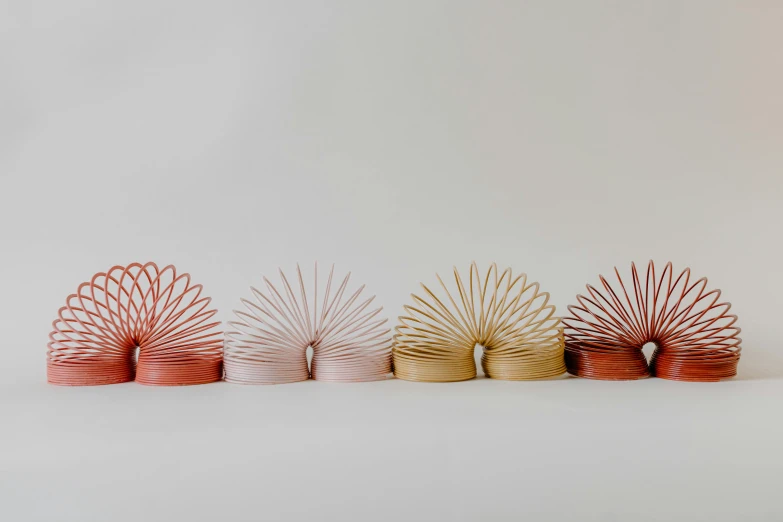 a row of wooden slink toys sitting next to each other, inspired by Ai Weiwei, trending on unsplash, kinetic art, gradient pink, copper wire, fronds, red oval turban