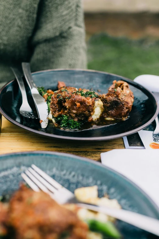 a person sitting at a table with a plate of food, by Jessie Algie, unsplash, pork, “ iron bark, exterior shot, stew