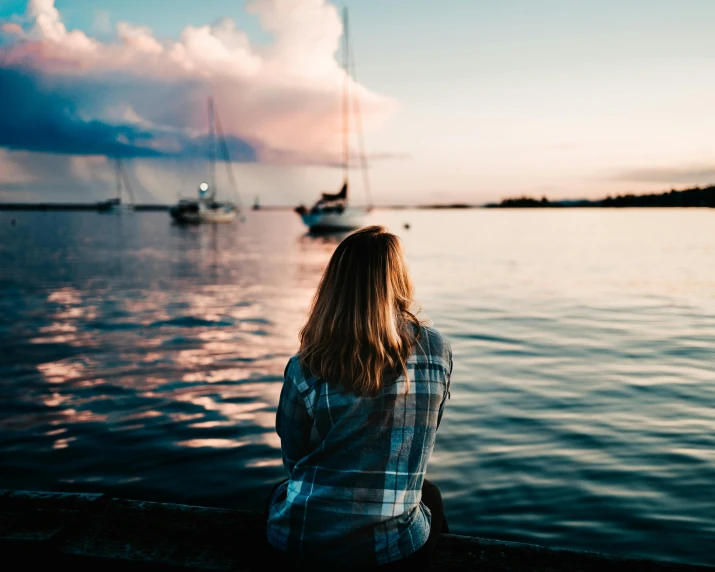 a woman sitting on a dock looking out at the water, pexels contest winner, happening, early evening, with water and boats, teenage girl, sittin