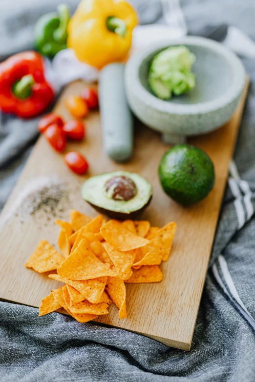 a wooden cutting board topped with tortilla chips, a still life, pexels, avacado chairs, dark grey and orange colours, square, medium portrait