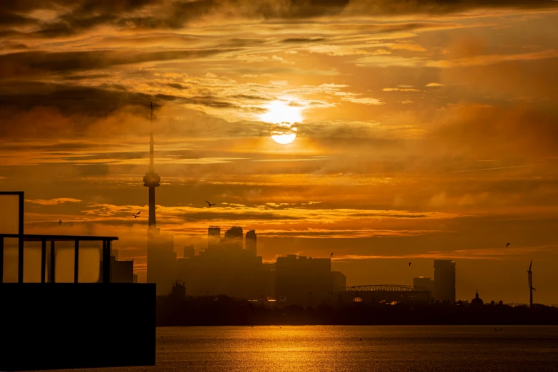 a large body of water with a city in the background, by Sebastian Spreng, pexels contest winner, sun shafts, toronto city, golden mist, empire silhouette