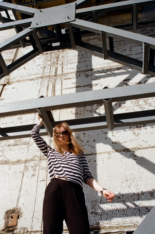 a woman standing in front of a metal structure, inspired by Alexander Rodchenko, unsplash, minimalism, wearing stripe shirt, designer sunglasses, sitting under bridge, wearing casual clothing