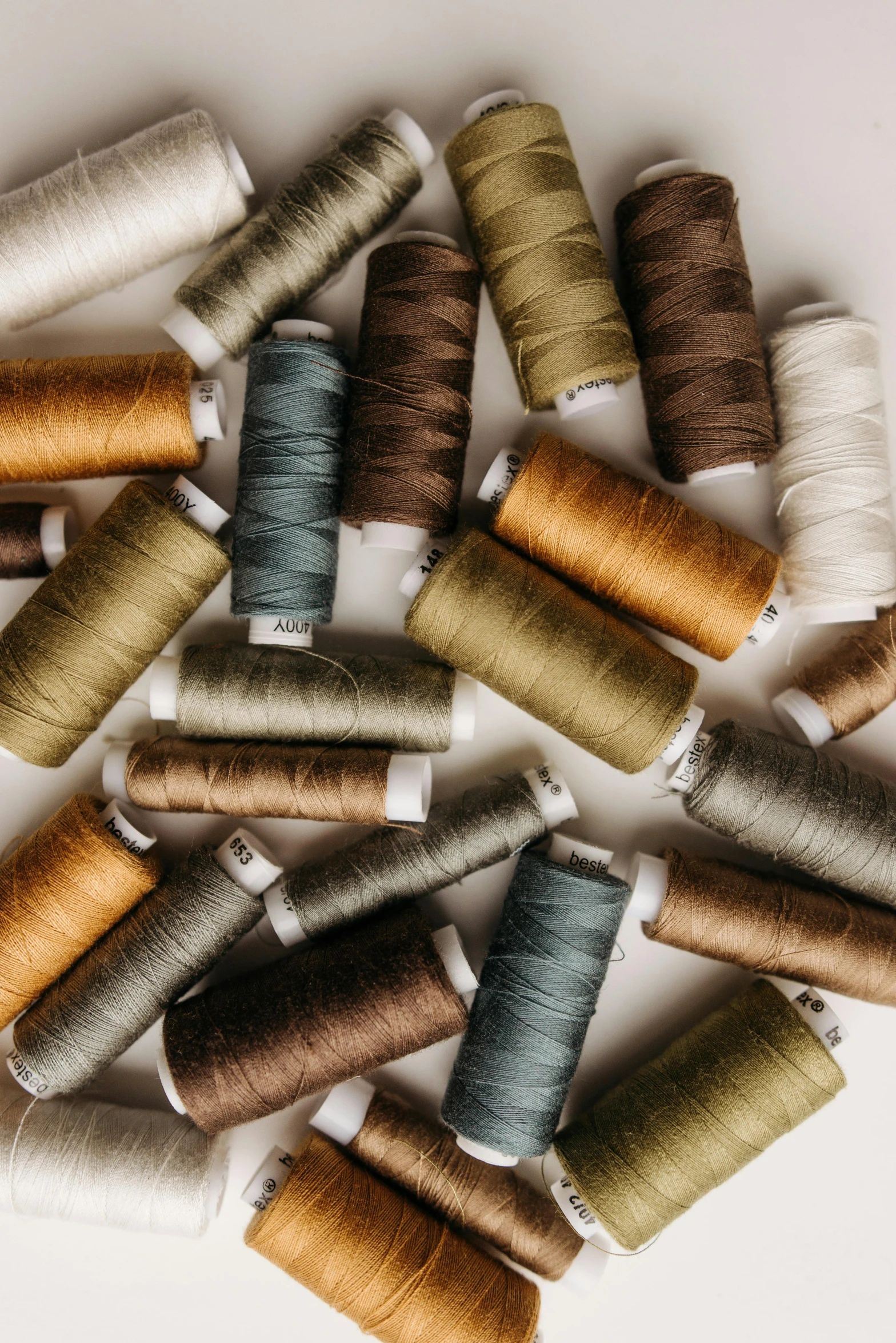 a bunch of spools of thread on a white surface, by Winona Nelson, trending on unsplash, arts and crafts movement, dark earthy colours, thumbnail, tailored clothing, digital image