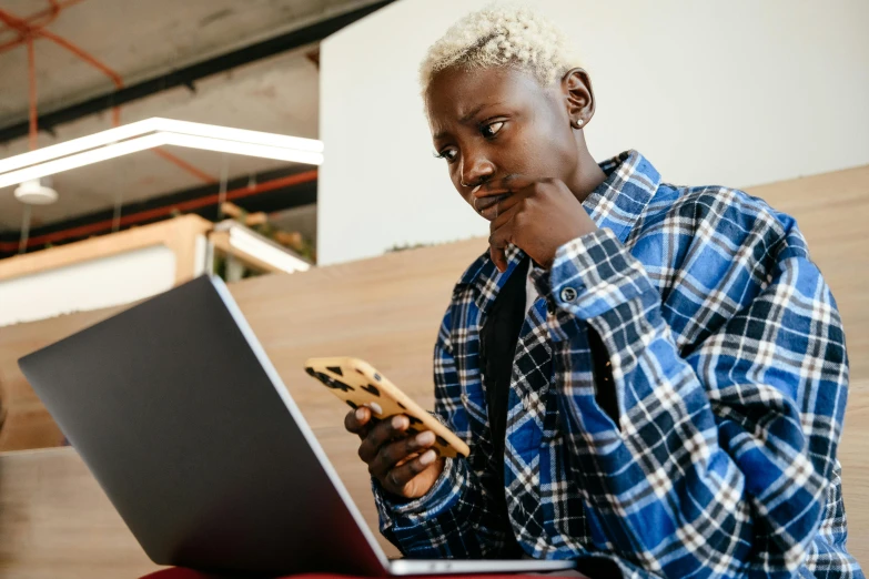 a man sitting in front of a laptop with a cookie in his hand, by Carey Morris, trending on pexels, afrofuturism, checking her phone, short blonde afro, looking confused, studious