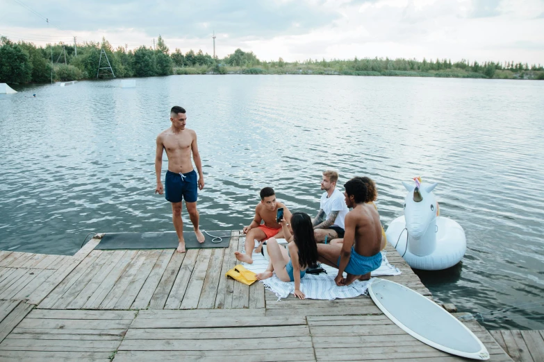 a group of people sitting on a dock next to a body of water, a picture, standing on surfboards, kacper niepokolczycki, airbnb, tarmo juhola