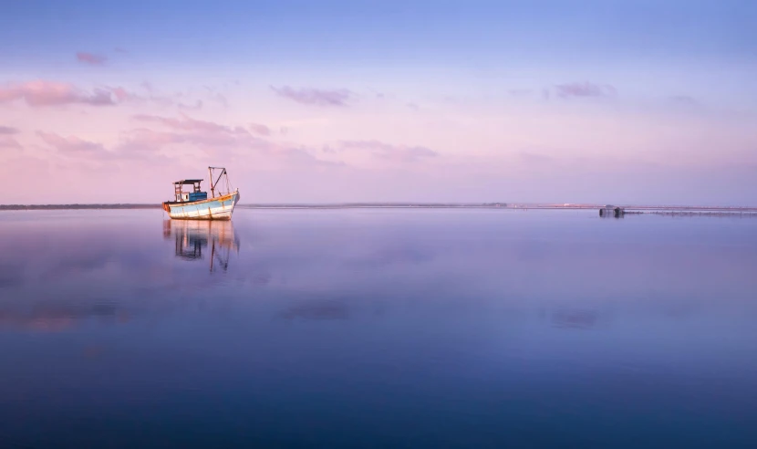 a boat sitting on top of a large body of water, a picture, by Peter Churcher, unsplash contest winner, pastel blues and pinks, calm evening, afar, panoramic shot