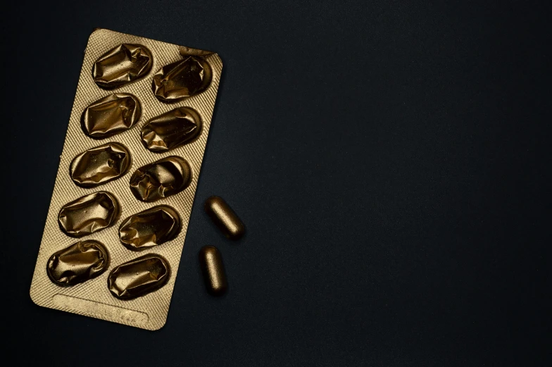 gold pills in a blister pack on a black background, by Julia Pishtar, orelsan, on grey background, deep colour, ignant