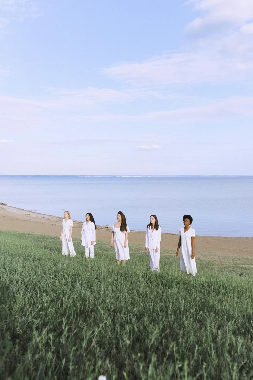 a group of people standing on top of a lush green field, an album cover, inspired by Pierre Puvis de Chavannes, unsplash, white uniform, shoreline, young women, rhode island