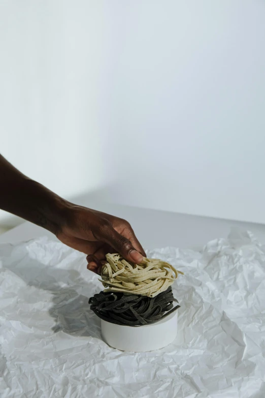 a person putting noodles in a bowl on a table, by Alison Geissler, adut akech, low detail, grey, vanilla