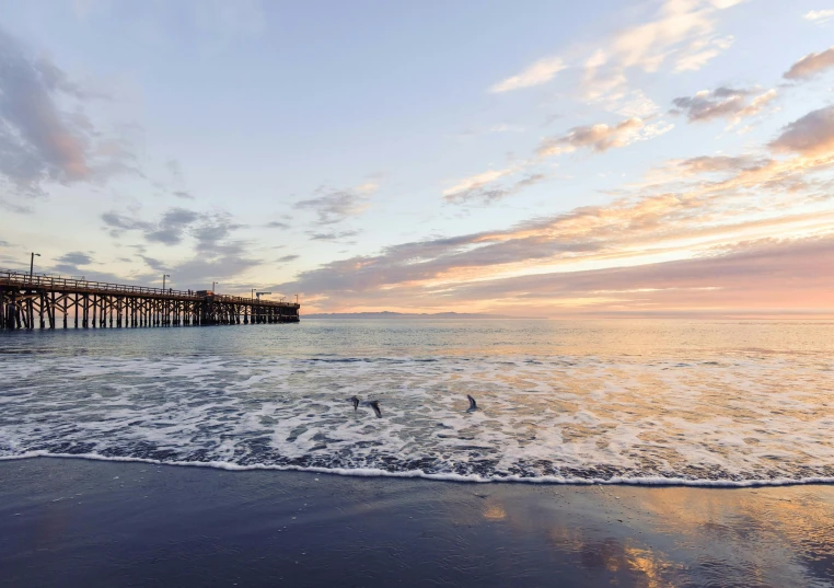 a body of water with a pier in the background, by Winona Nelson, pexels contest winner, on the beach at sunset, central california, maryport, hd footage