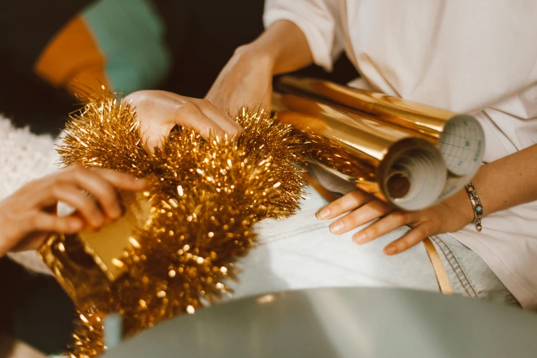a close up of a person cutting tinsel, an album cover, by Julia Pishtar, pexels contest winner, arts and crafts movement, brown and gold color palette, giving gifts to people, plastic wrap, gold