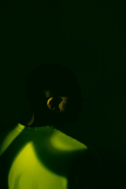 a man holding a tennis racquet in a dark room, an album cover, by artist, pexels, afrofuturism, yellow and green, difraction from back light, shadowed face, scene from a rave