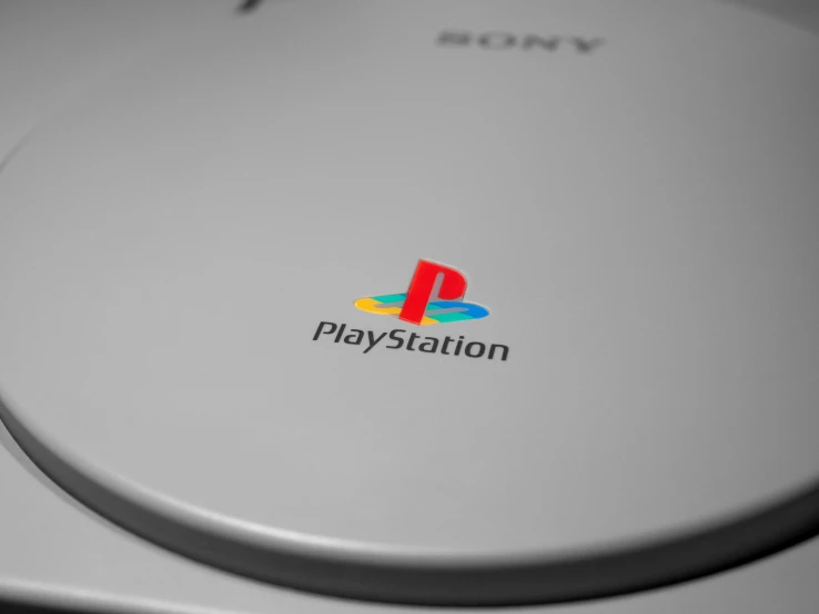 a sony playstation game console sitting on top of a table, an ambient occlusion render, postminimalism, high angle close up shot, multicoloured, grey metal body, logos