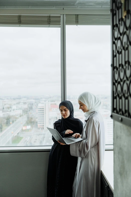 two women standing next to each other in front of a window, trending on unsplash, hurufiyya, cybermosque interior, holding notebook, high angle, tech city in the background